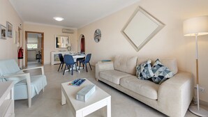 Una sala de estar con un sofá, una mesa de centro, un comedor con sillas, una cocina al fondo y un espejo grande en la pared.