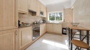 Una cocina con armarios de madera, un horno de acero inoxidable, un microondas y una ventana con persianas.
