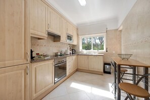 A kitchen with wooden cabinets, a stainless steel oven, a microwave, and a window with blinds.