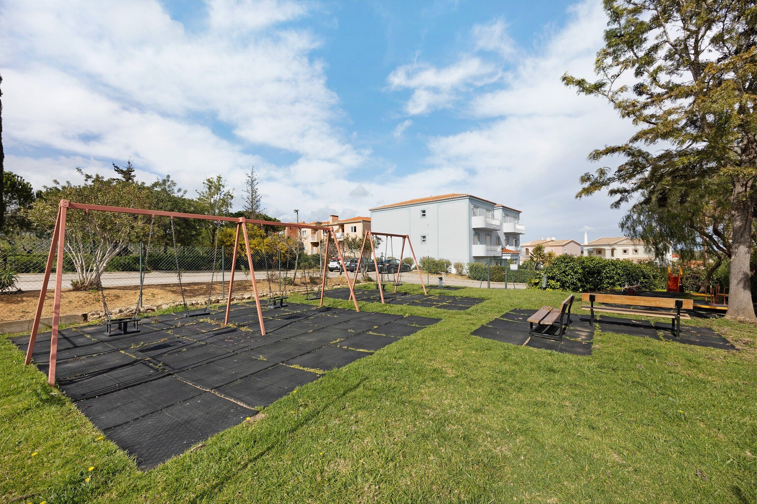 A park with a swing set, benches, and a building in the background.