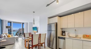 A modern apartment with a dining area, kitchen, and a large window overlooking a cityscape. - Stylish 1BR Apartment Near Beach (Hallandale Beach)