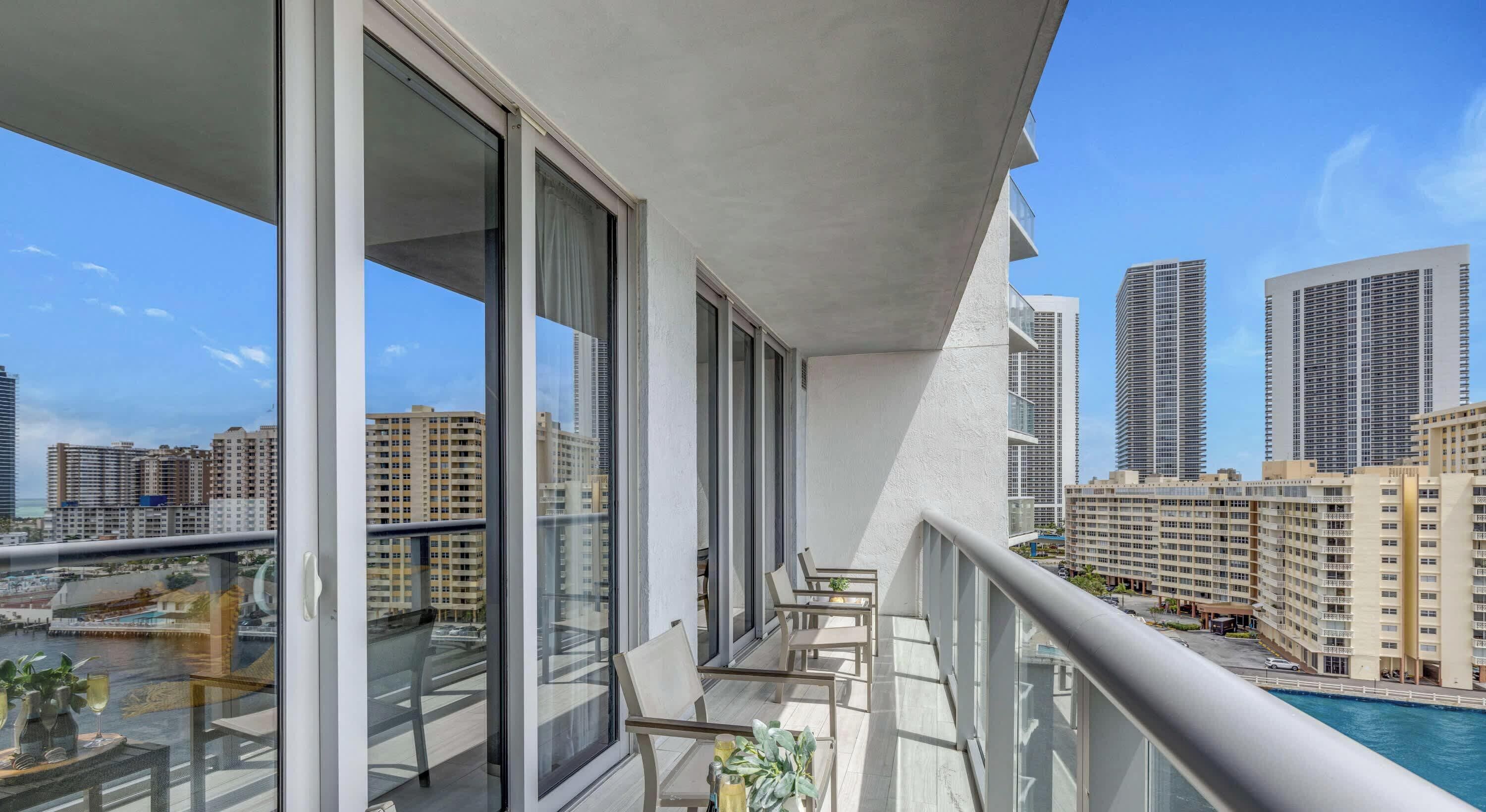 A balcony with large windows, a pool, and a cityscape view.