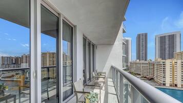 A balcony with large windows, a pool, and a cityscape view.