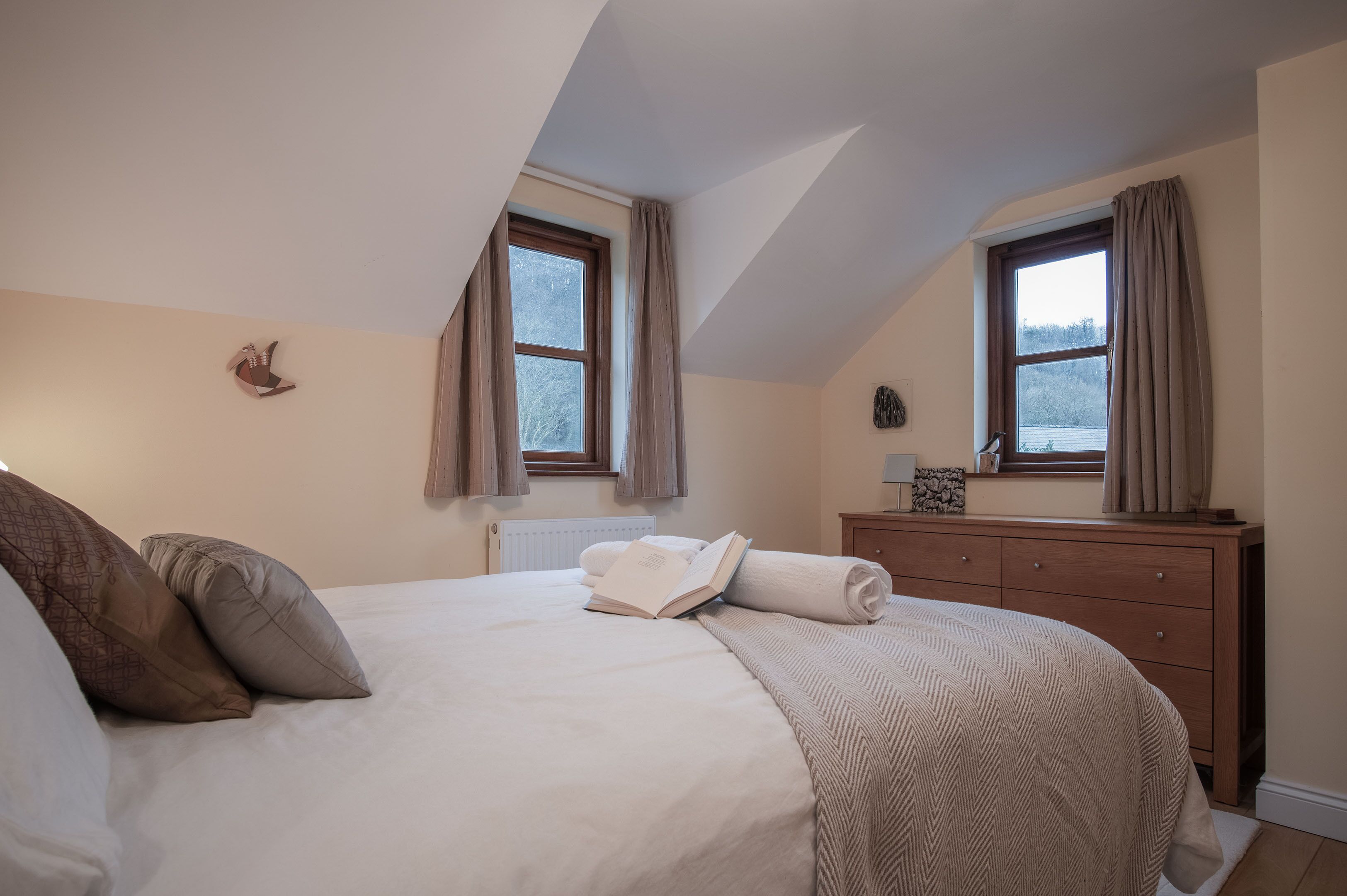 A bedroom with a bed, two windows, a dresser, and a radiator.