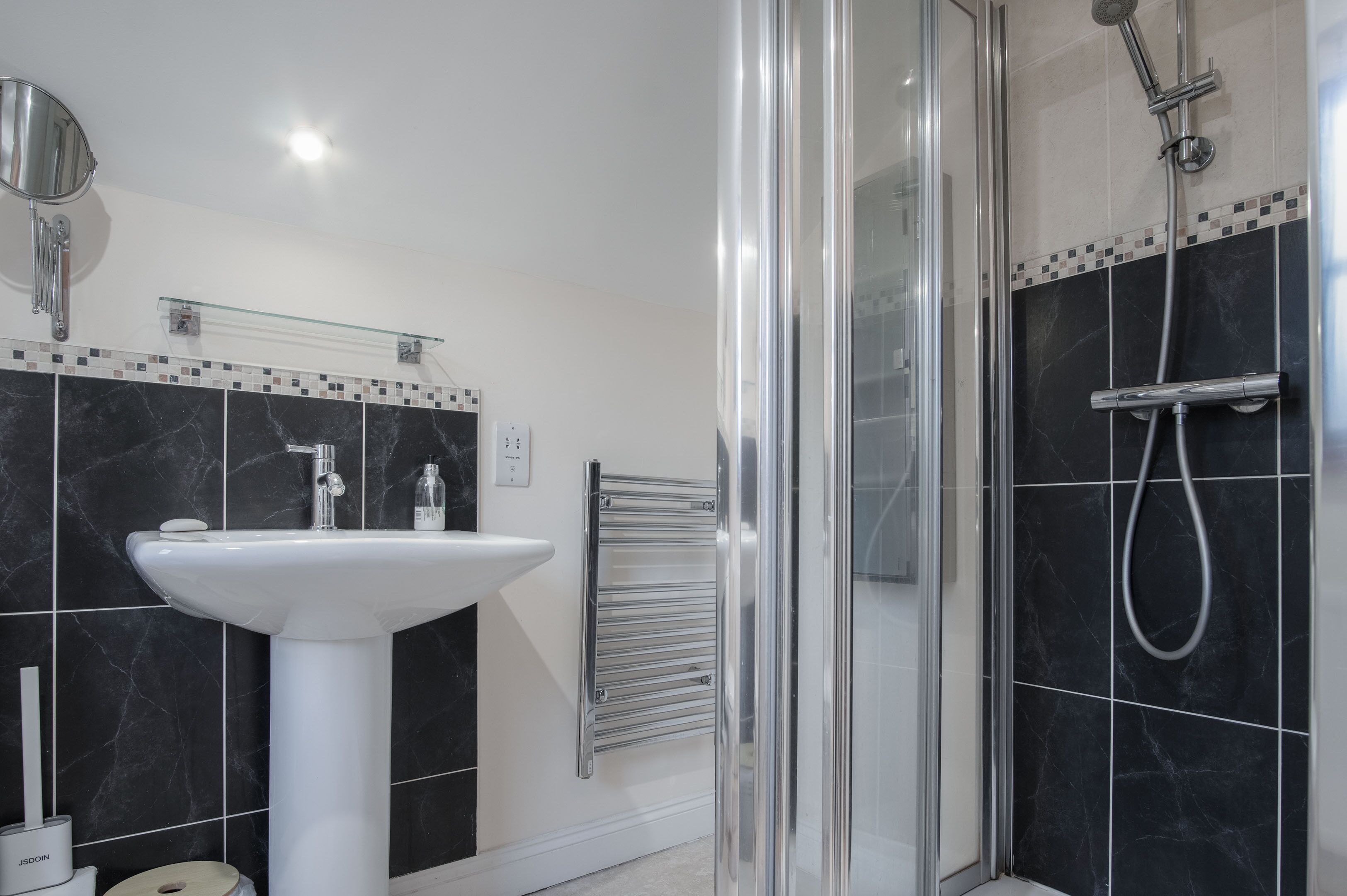 Un baño moderno con un lavamanos pedestal blanco, una cabina de ducha con paredes de vidrio y un salpicadero de azulejos.