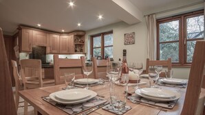 A dining area with a wooden table set for six, surrounded by wooden chairs. - Llais Afon - 3 Bedroom Holiday Home - Fishguard (Fishguard)