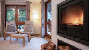 A cozy living room with a fireplace, two upholstered chairs, a floor lamp, and a large TV screen. - Llais Afon - 3 Bedroom Holiday Home - Fishguard (Fishguard)