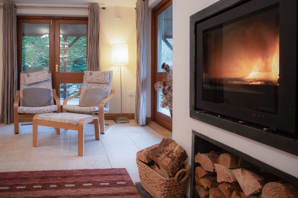A cozy living room with a fireplace, two upholstered chairs, a floor lamp, and a large TV screen. - Llais Afon - 3 Bedroom Holiday Home - Fishguard (Fishguard)