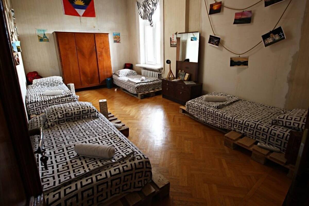 Habitación tipo dormitorio con tres camas, suelo de madera, un armario, un espejo y adornos en la pared, incluyendo fotografías y una bandera.