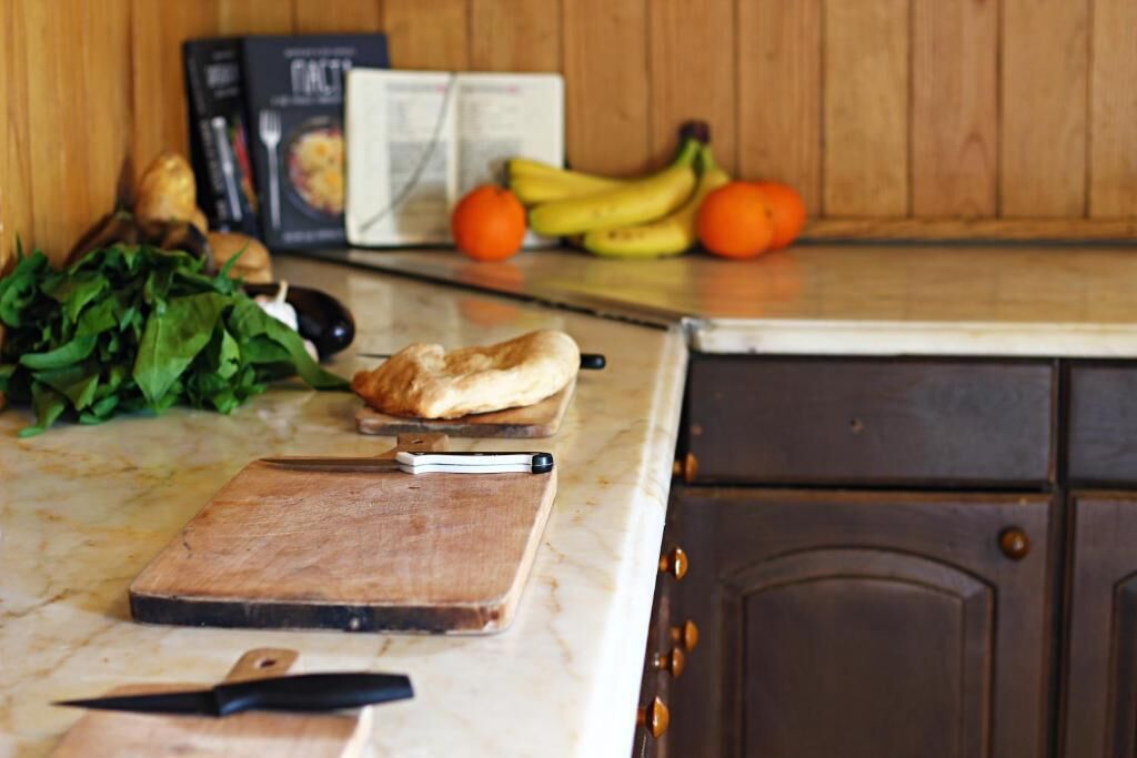 A kitchen counter with a cutting board, a knife, a loaf of bread, and some vegetables.