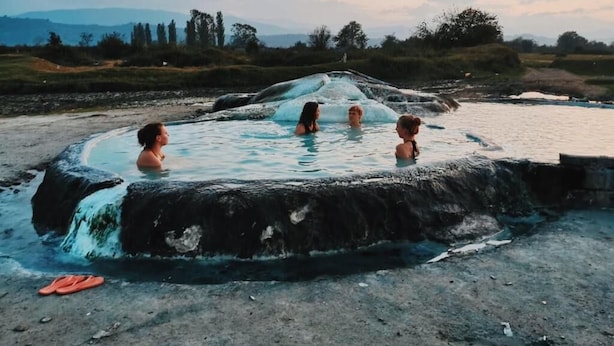 Eine heiße Quelle mit drei Personen im Wasser, eingebettet in eine natürliche Landschaft.