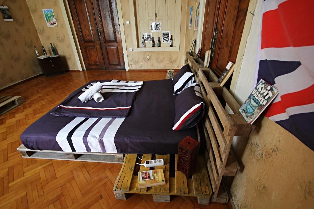 Una cama con una colcha azul y blanca a rayas, un cabecero de madera y una pequeña mesita con un libro y un control remoto.