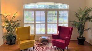 A room with a large bay window, two chairs, a small round table, and two potted plants. - Paradise Bound - Great Prices, Heated Pool, 5 Min to Beaches (Bradenton)