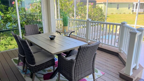 A covered outdoor patio with a wooden table and wicker chairs, a small table with a bowl, and a potted plant. - Paradise Bound - Great Prices, Heated Pool, 5 Min to Beaches (Bradenton)