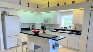 A modern kitchen with white cabinets, a central island with seating, a microwave, and a refrigerator. - Paradise Bound - Great Prices, Heated Pool, 5 Min to Beaches (Bradenton)