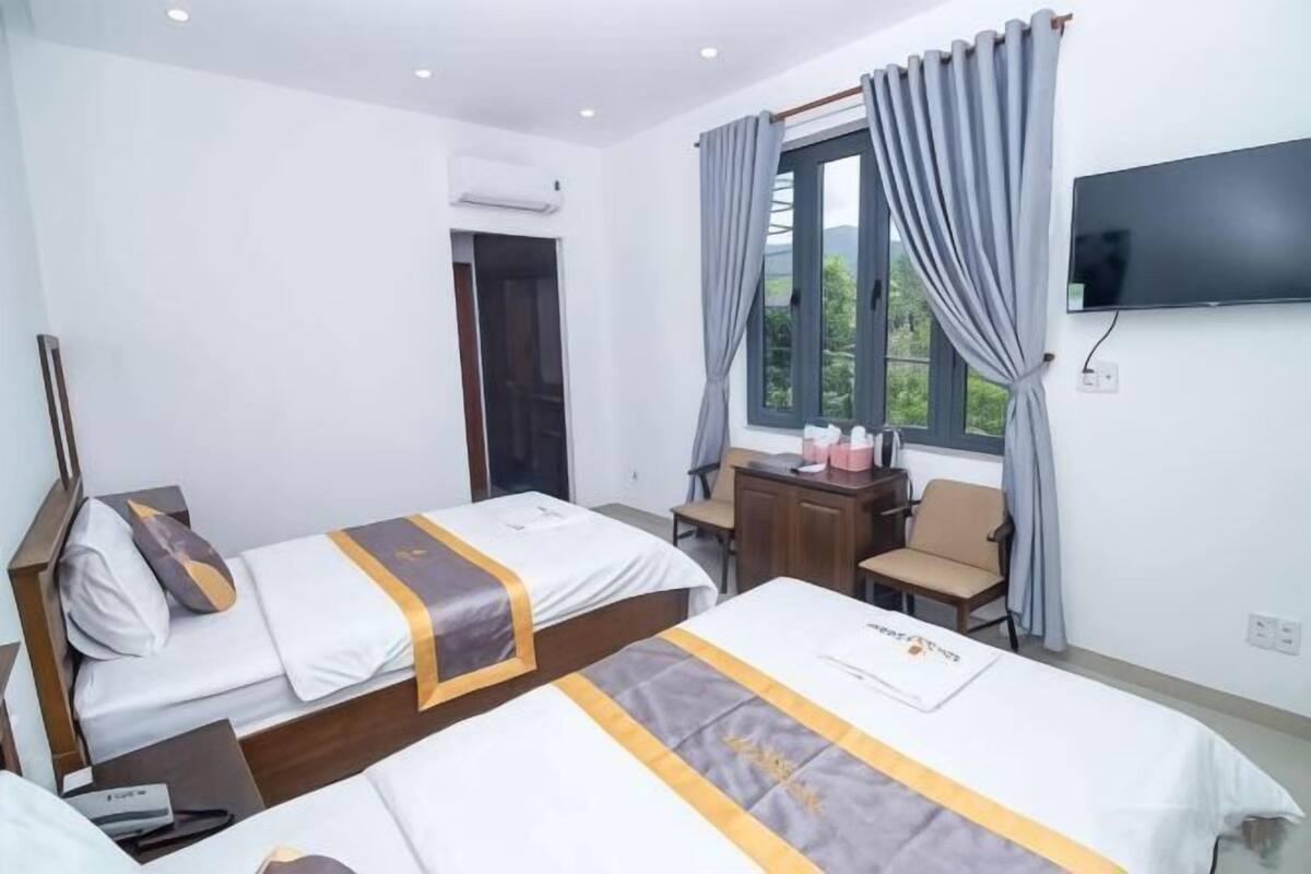A hotel room with two beds, a desk, a chair, a TV, and a window with curtains.