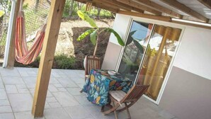 A covered patio area with a table and chairs, a hammock, and a view of a garden. - Bélya - Peaceful gîte with terrace and sea view (Le Vauclin)