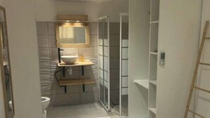 A narrow, modern bathroom with a toilet, sink, and mirror. There are built-in shelves and a ladder leaning against the wall. - Bélya - Peaceful gîte with terrace and sea view (Le Vauclin)