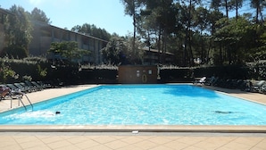 Une piscine avec une terrasse carrelée, entourée de chaises longues et d’un bâtiment en arrière-plan.