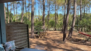 Un espace extérieur abrité, avec une table et des chaises, entouré d’un paysage boisé.