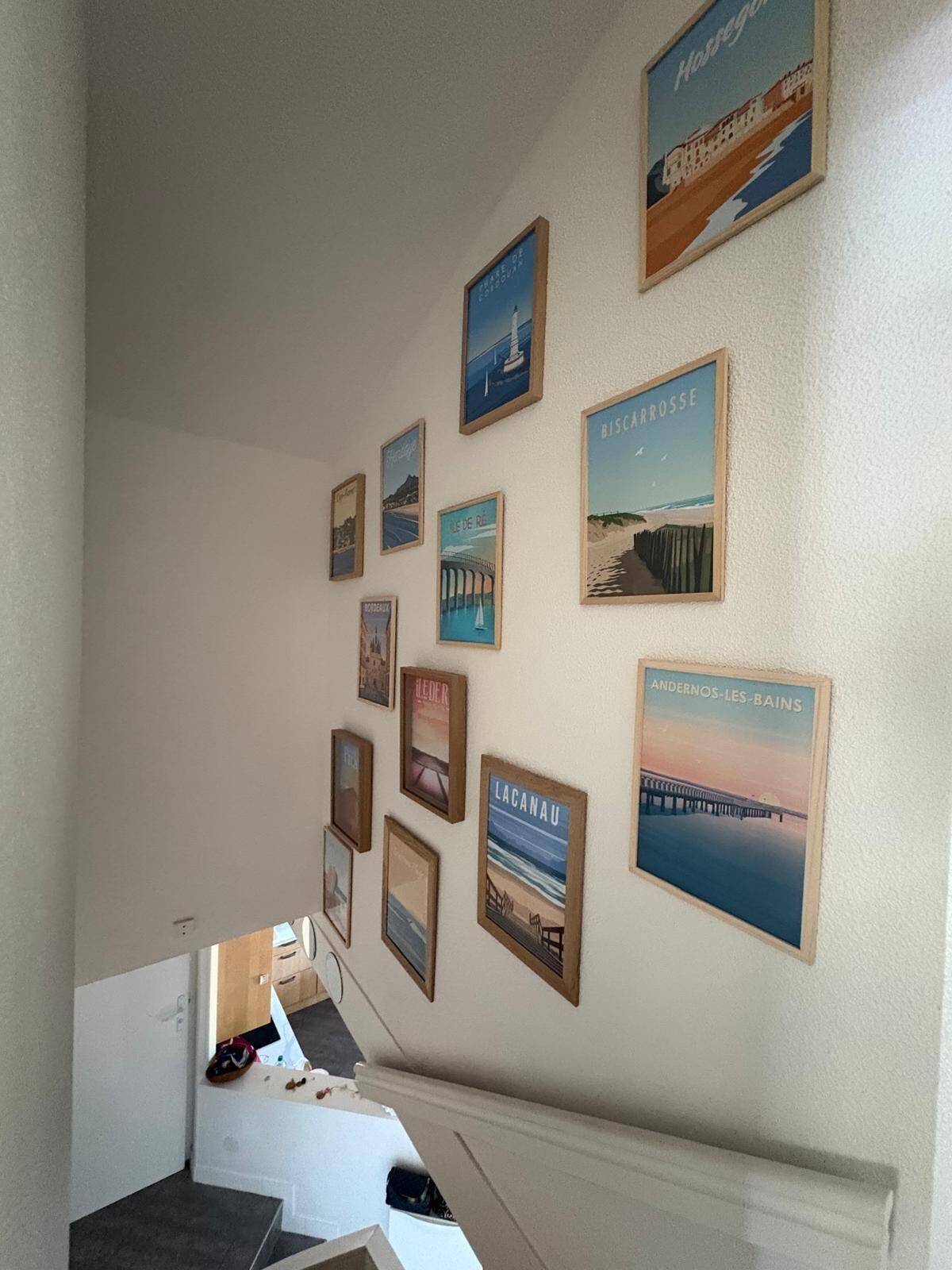 Un couloir avec un escalier menant à un autre étage, dont les murs sont ornés de divers tableaux encadrés.