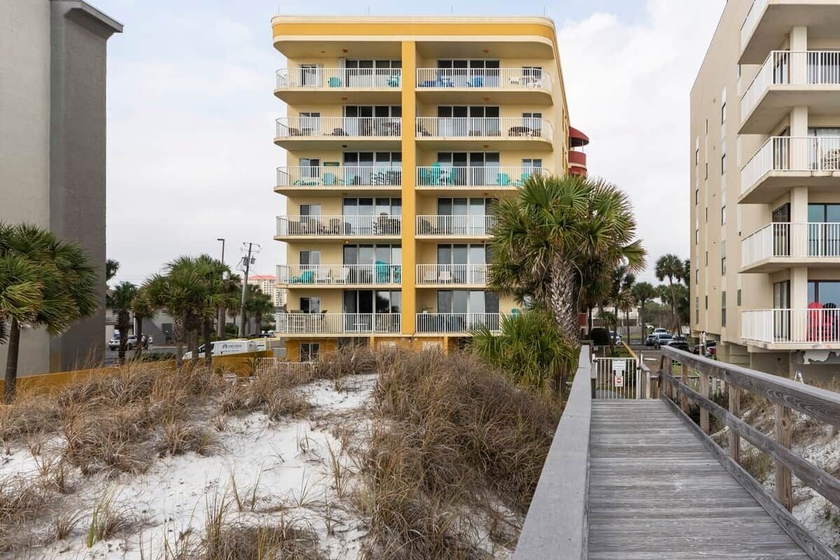 Un hotel de varios pisos con balcones, un paseo marítimo de madera y una playa arenosa al frente.