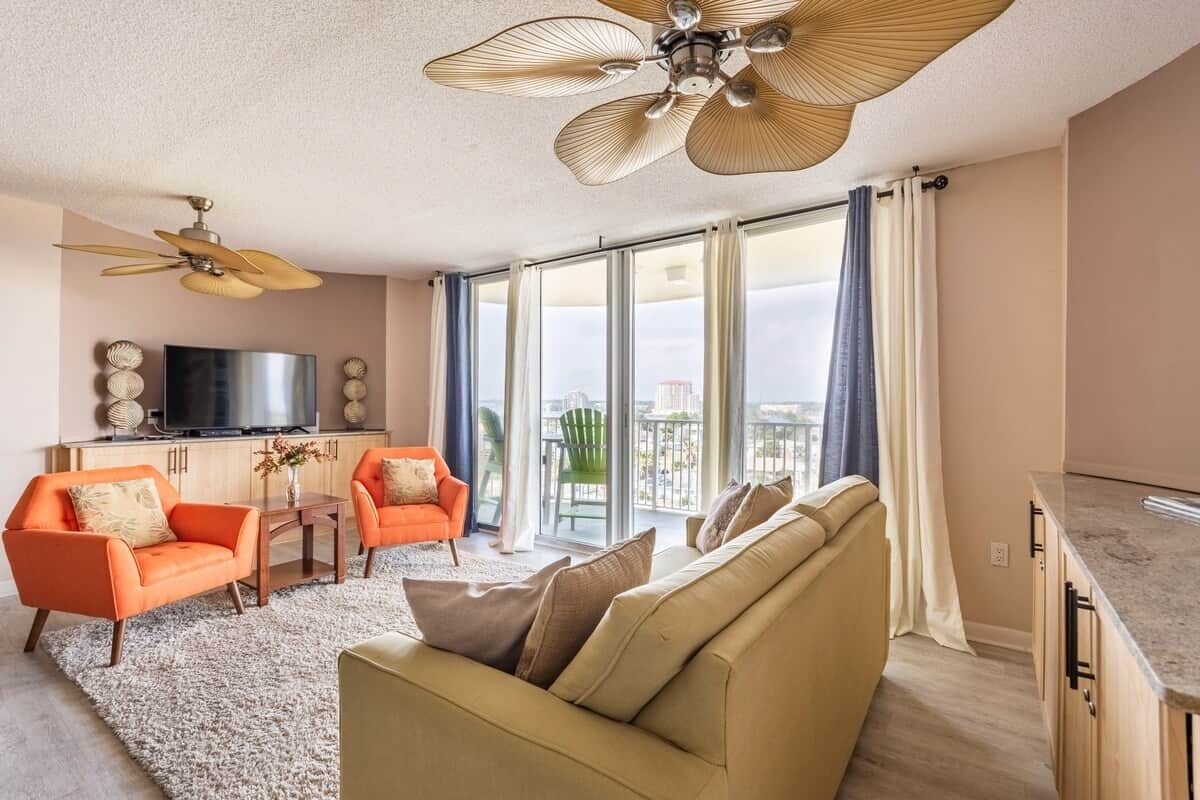 Un'ampia zona giorno con un divano color beige, poltrone arancioni, una TV a schermo piatto e una ventola a soffitto.
