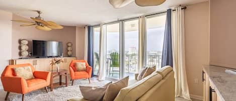 Ett rymligt vardagsrum med en beige soffa, orange fåtöljer, en platt-TV och en takfläkt.