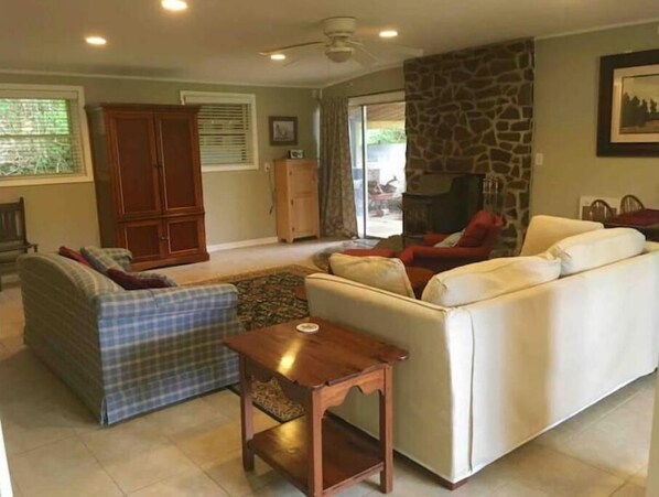 Uma sala de estar com sofá, uma poltrona xadrez, uma mesa de madeira e uma parede de destaque em pedra.