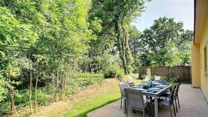 An outdoor patio with a table and chairs, surrounded by lush greenery and trees. - House near beaches, classified 3*- quiet (Névez)