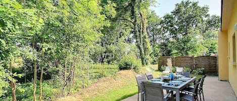 An outdoor patio with a table and chairs, surrounded by lush greenery and trees.