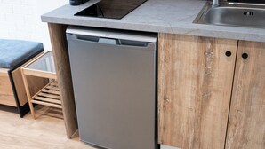 A compact kitchen with a built-in dishwasher, a wooden cabinet, and a stainless steel sink. - Cozy modern studio in Thessaloniki (Thessaloniki)