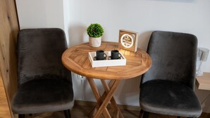 Two dark grey upholstered chairs around a small wooden table with a tray holding two black cups. A potted plant and a framed sign are on the table. - Cozy modern studio in Thessaloniki (Thessaloniki)