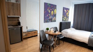 A compact hotel room with a bed, a small dining table with chairs, a kitchenette, and a large window with curtains. - Cozy modern studio in Thessaloniki (Thessaloniki)