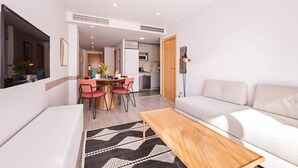 A modern living room with a sofa, a wooden coffee table, and a dining area with a table and chairs. - Sweett | Fira 104 - Two Bedroom Apartment, Sleeps 4 (Barcelona)