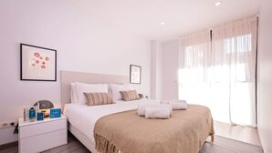 A hotel room with a bed, a nightstand, a lamp, and a window with sheer curtains. - Sweett | Fira 104 - Two Bedroom Apartment, Sleeps 4 (Barcelona)