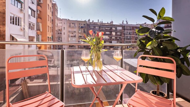 Een balkon met twee roze stoelen, een tafel en een vaas met bloemen.