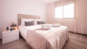 Een hotelkamer met een bed, nachtkastje, lamp en een raam met gordijnen.