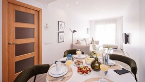 Un coin repas avec une table dressée pour quatre personnes, comprenant des assiettes, des couverts et un plateau de fruits.