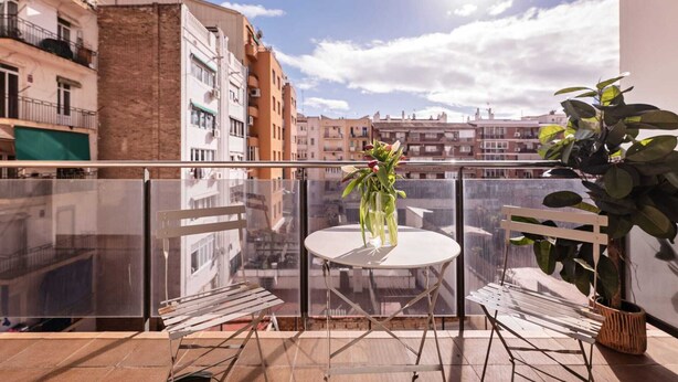 A balcony with a round table and two chairs, a potted plant, and a view of surrounding buildings. - Sweett | Fira 304 - Two Bedroom Apartment, Sleeps 5 (Barcelona)