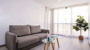 Ein modernes Wohnzimmer mit einem grauen Sofa, einem Glastisch und einer Topfpflanze.