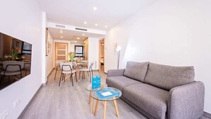 Een moderne woonkamer met een grijze bank, een glazen salontafel, en een eethoek met een houten tafel en stoelen.