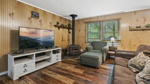 Un salon chaleureux avec un mur lambrissé en bois, un téléviseur, un canapé, un fauteuil et une cheminée.