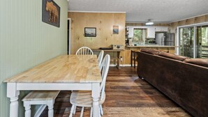 Un coin repas avec une table et des chaises en bois, un canapé marron et une cuisine en arrière-plan.