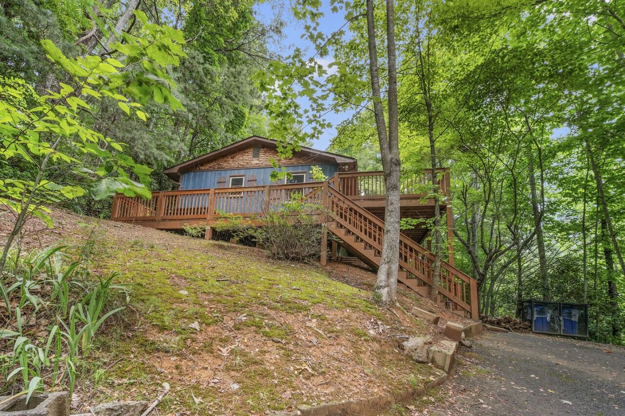 A cabin with a wooden deck and stairs, surrounded by dense forest.