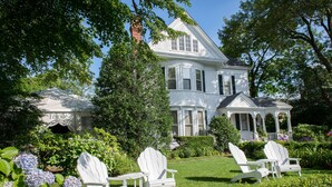A large white house with a porch and a garden with hydrangeas and white chairs. - The Coco, The Edgartown Collection (Edgartown)