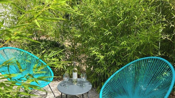 Un patio con dos sillas metálicas turquesas y una pequeña mesa redonda con una botella y vasos.