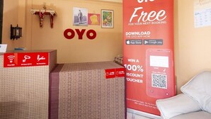 A hotel room with a bed, a red OYO promotional poster, and a wall-mounted fan. - OYO 325 Naiyang Cottage (Sa Khu)
