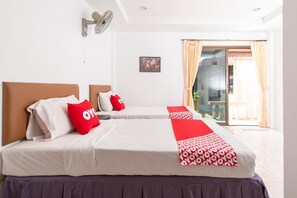 Two beds with headboards and pillows, surrounded by a sliding glass door leading to a balcony with a view.