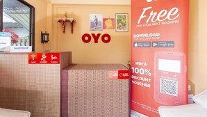 A hotel reception area with a large 'OYO' sign, a promotional poster for a free booking, and a QR code for a discount voucher.